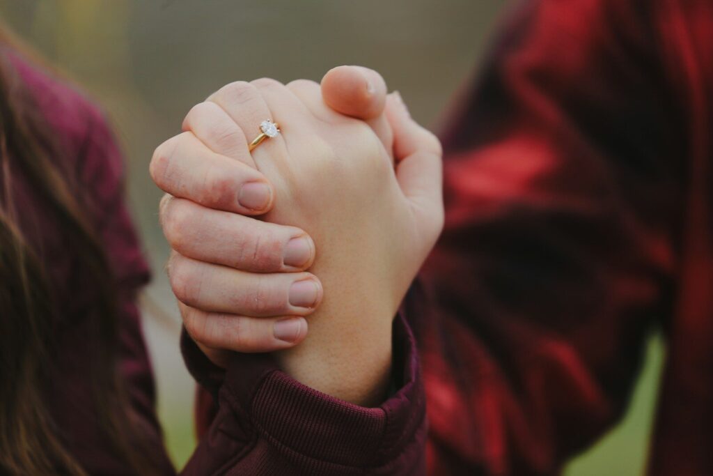 Two people holding hands with a gold diamond ring on one finger